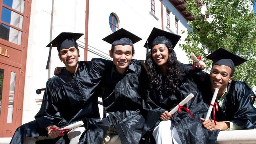 graduates in black caps and gowns sitting outside of college